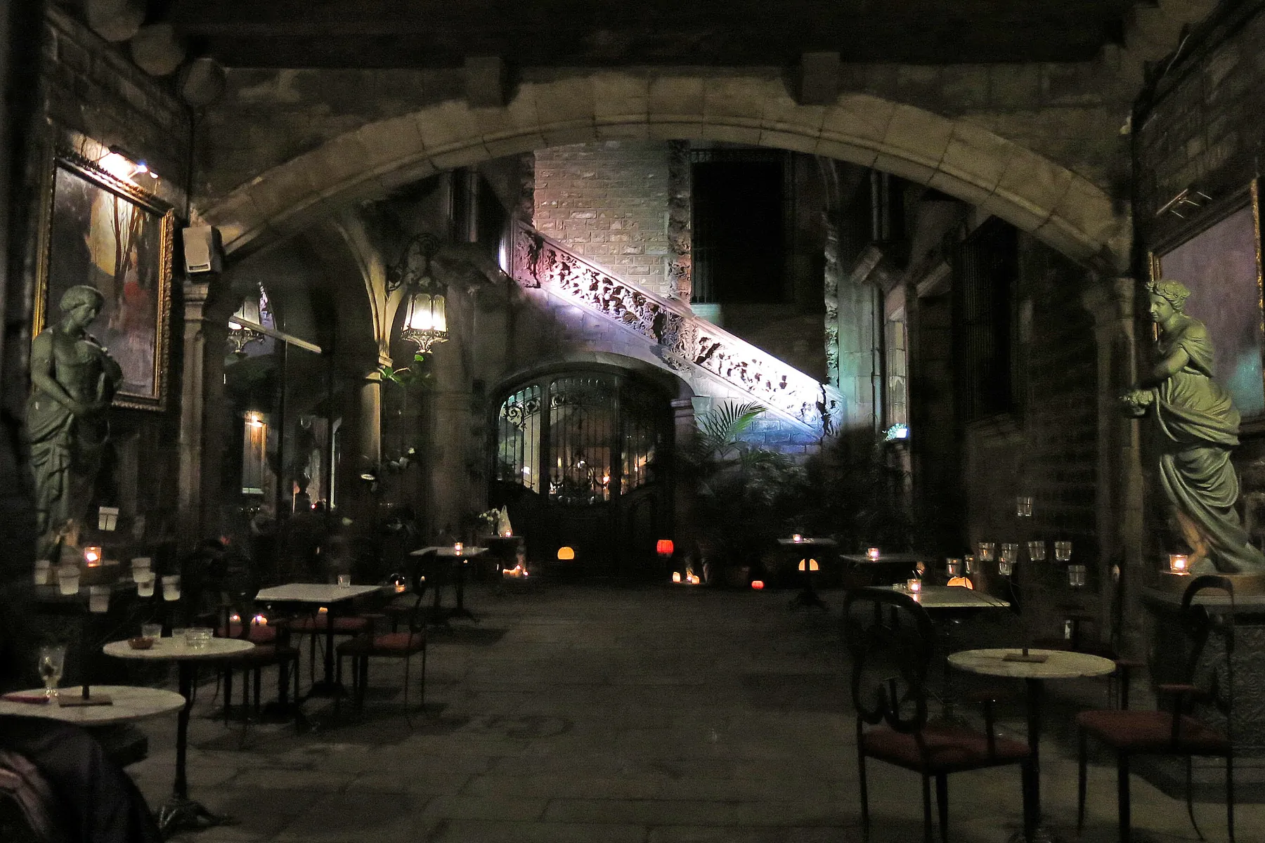 The courtyard of Palau Dalmases at night, with candlelit tables under stone arches and statues on either side