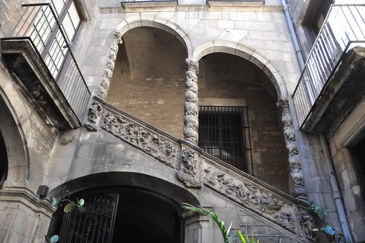 The stone staircase of Palau Dalmases rising under two ramping arches on twisted columns, with a carved balustrade