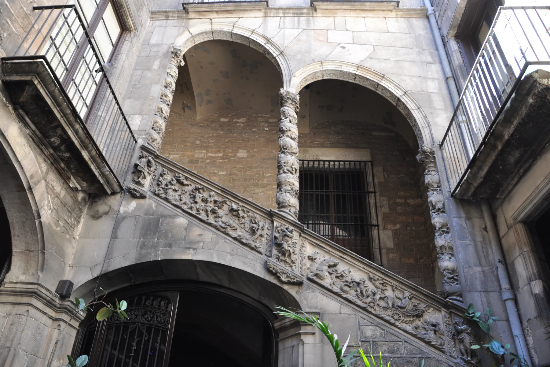 The stone staircase of Palau Dalmases rising under two ramping arches on twisted columns, with a carved balustrade